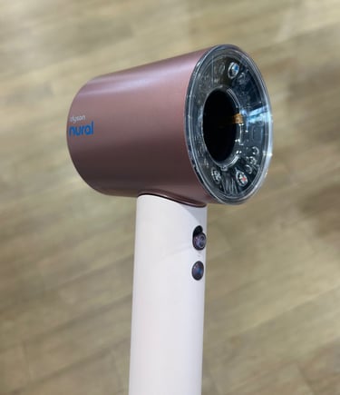 Dyson Supersonic Nural hair dryer in blush pink with clear ring light sensor on wood background.