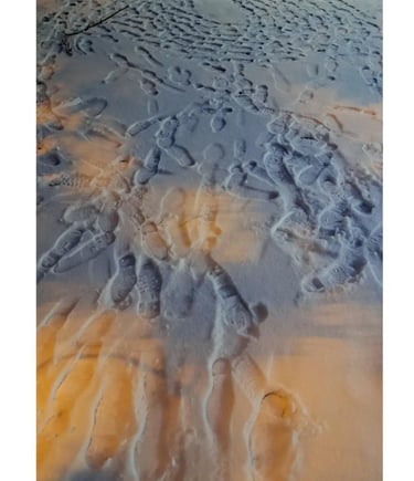 Boot footprints forming circular patterns in fresh snow illuminated by golden sunset light.