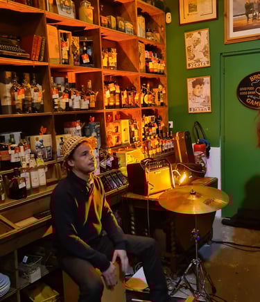 A musician plays a cajon drum during a live session in a cozy Irish pub with whiskey shelves.