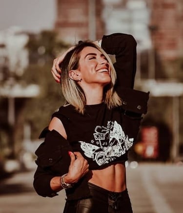 Una mujer sonriente con una camiseta corta negra estampada y una chaqueta vaquera posa al aire libre