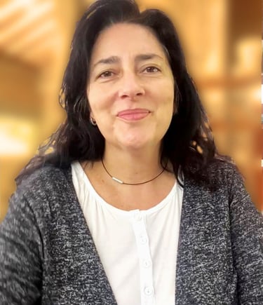Smiling woman with long dark hair wearing a grey cardigan and white blouse in a professional setting.