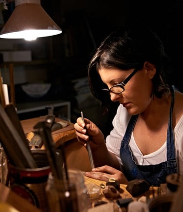 Artesana joyera en su mesa de trabajo, usando herramientas para crear piezas de joyería
