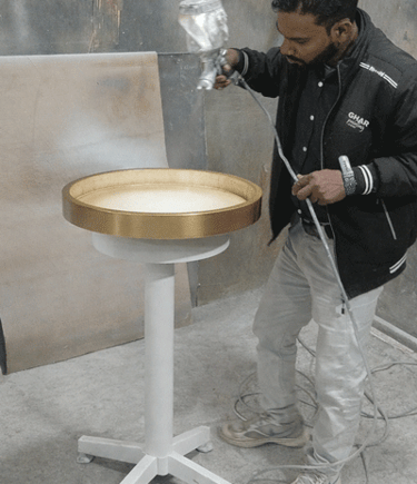 Professional painter applying a gold finish to a circular metal table using a spray gun.