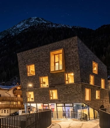 A modern, geometrically designed building with illuminated windows at night, situated in a snowy ski