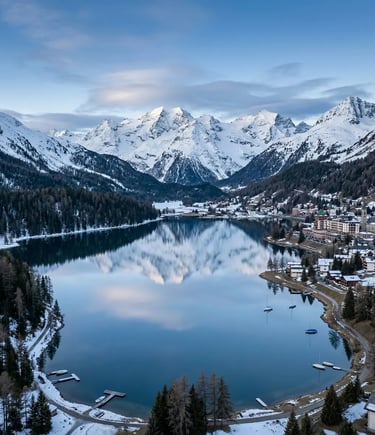  Drone shot of St. Moritz lake reflecting snowcapped peaks with alpine village on the shore