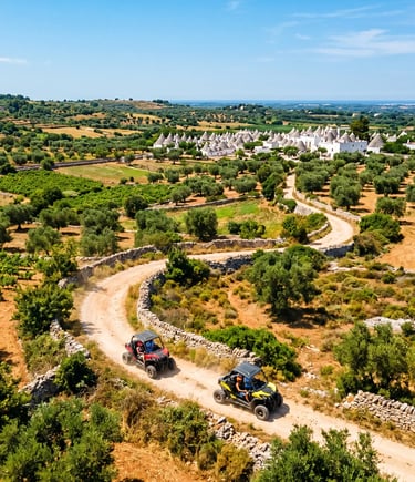 Aerial view of two buggies on winding dirt trail through Itria Valley with trulli in background