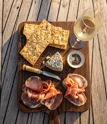 Overhead view of rosemary crackers, cheese, cured meat and white wine on yacht deck