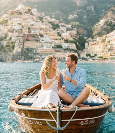 Couple toasting prosecco on a wooden boat with Positano village in the background