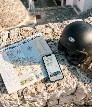 Valle d'Itria travel map, GetYourGuide booking on smartphone, and buggy helmet on limestone wall