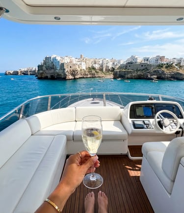 Flybridge view of Polignano a Mare with prosecco glass, white leather seating and teak deck