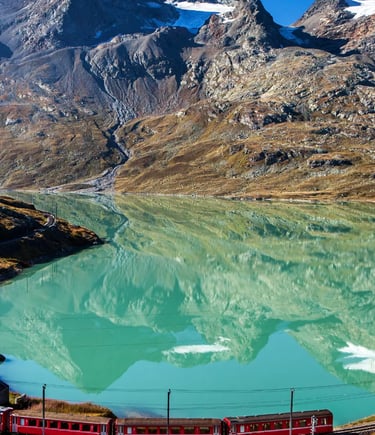 Red Bernina Express train passing turquoise alpine lake with mountain reflections