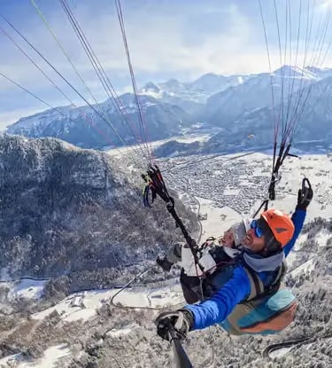Top-down view of tandem paragliders flying over a frozen forest in Jungfrau Region