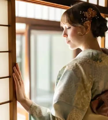 Woman in soft blue kimono with golden hair pin gazing through traditional shoji screen