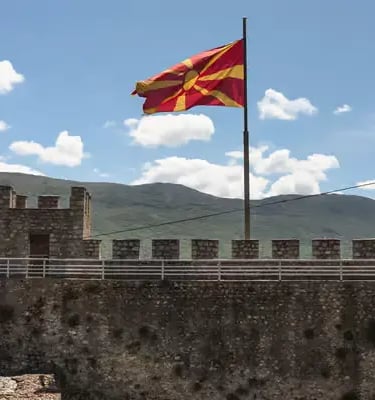 North Macedonia national flag waving on stone fortress walls with mountains and blue sky Ohrid