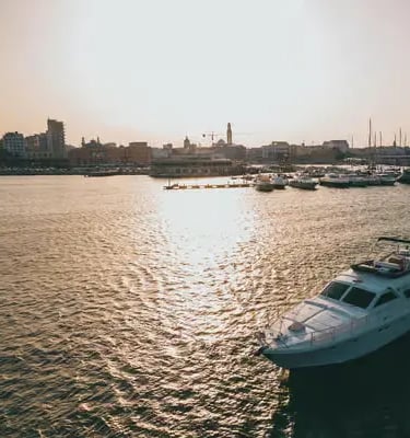 Bari harbor at sunset with boats and city skyline reflecting on calm Adriatic water
