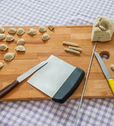 Freshly shaped orecchiette pasta with dough and knives on board at Lecce cooking class
