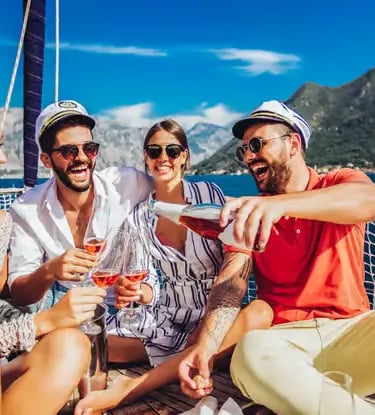 Four friends laughing and enjoying complimentary drinks on a boat tour along the Amalfi Coast