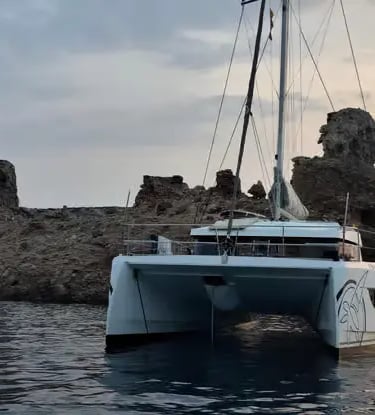 Luxury catamaran anchored beside dramatic limestone cliffs at sunset Menorca