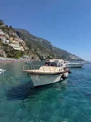 Traditional Gozzo tour boat anchored in turquoise water off Positano coastline