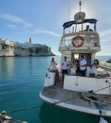 Yacht crew and guests onboard luxury boat with Polignano a Mare cliffside town in background