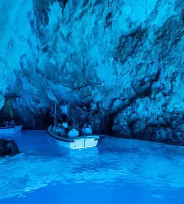 Glowing blue interior of Biševo Blue Cave with small tour boat inside, Croatia