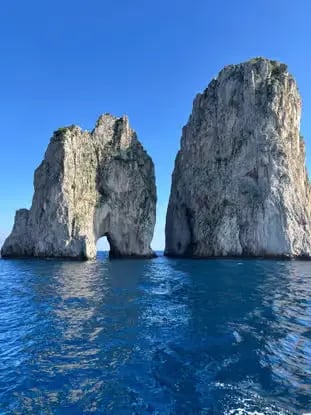 Iconic Faraglioni rocks of Capri rising from the deep blue Tyrrhenian Sea on a clear summer day.
