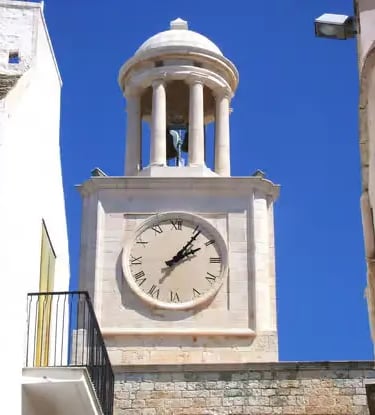  White limestone clock tower in historic center of Locorotondo against clear blue Puglia sky