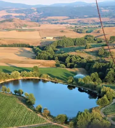 Aerial view of green fields, small lake and rolling hills seen from a hot air balloon in Italy