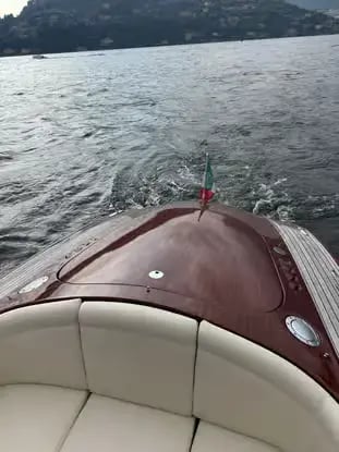  Polished wooden boat deck with Italian flag cruising on Lake Como private tour