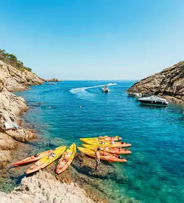 Colorful sea kayaks resting on a rocky shore inside a crystal clear Costa Brava cove