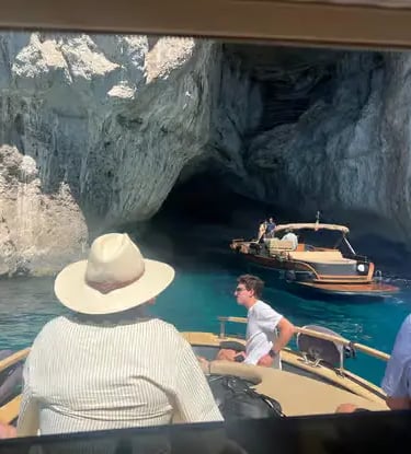 Small boat entering Blue Grotto cave in Capri with turquoise water and limestone cliffs
