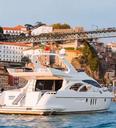 Private luxury yacht with Portuguese flag on Douro River beneath iconic Porto iron bridge.
