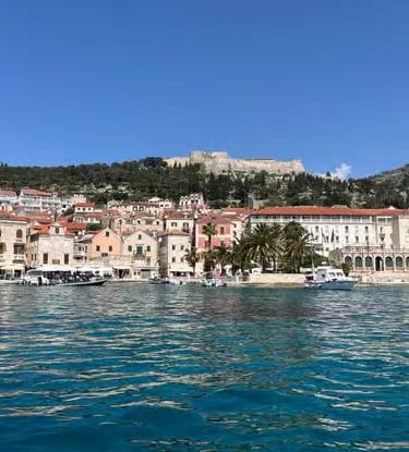 Hvar Town harbor with stone houses, palm tree and Spanish Fortress on hilltop above