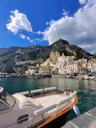  Traditional Gozzo boat moored in Amalfi harbor with colorful town and cliffs in background