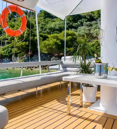 Teak deck lounge seating area on a Gulet with turquoise water and green coastline