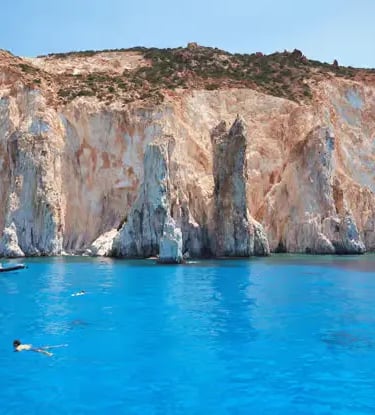 Kleftiko white volcanic cliffs and turquoise water in Milos Greece with swimmer and boats