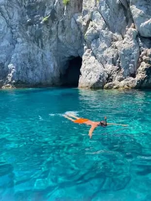 Snorkeler floating in crystal turquoise water near a Capri sea grotto during private boat tour