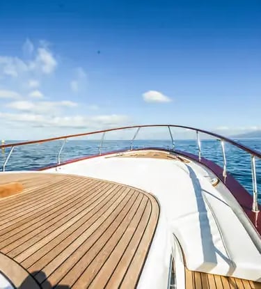 Teak deck bow of a Gozzo boat cruising toward the Amalfi coastline under blue sky