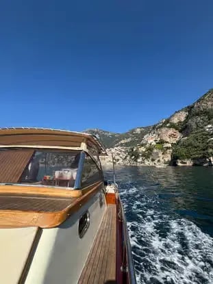 Traditional wooden Gozzo boat cruising along the Amalfi Coast cliffs on a clear day