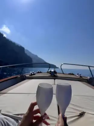 Two Prosecco glasses raised in a toast on a boat cruising the Positano coastline