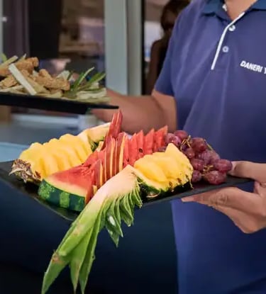 Crew serving fresh tropical fruit platter onboard Milos premium sailing tour