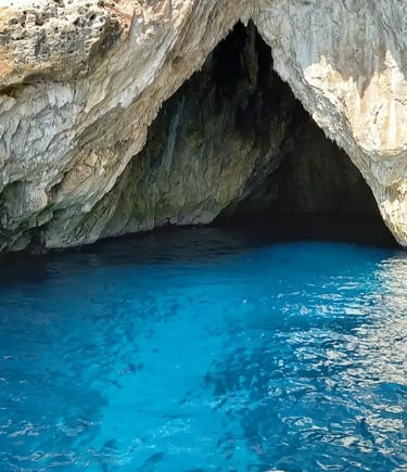 View from boat bow approaching dramatic limestone sea cave with electric blue water in Salento