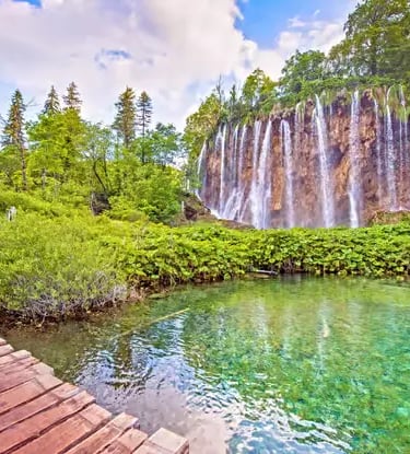 Wooden boardwalk along turquoise lake and waterfall at Plitvice, Croatia