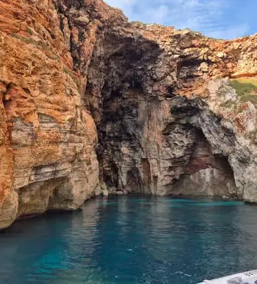 Turquoise water inside red limestone sea cave on Menorca southern coastline