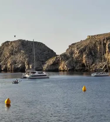 Catamarans and boats anchored in sheltered rocky bay along Menorca coast