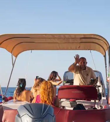 Smiling Italian boat captain waving with passengers on flexible Puglia coast tour at golden hour