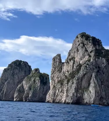 Faraglioni rock formations of Capri rising from the deep blue Tyrrhenian Sea, seen from a boat.
