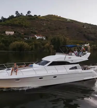 Private white motor yacht cruising calm Douro River with green vineyard hills behind