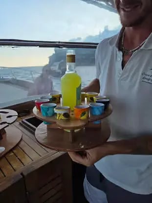 Crew member serving limoncello shots on wooden tray during Amalfi Coast boat tour