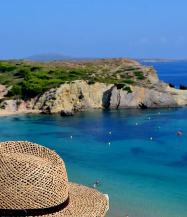 Straw hat on a ledge overlooking a turquoise beach and rocky coastline in Menorca, Spain